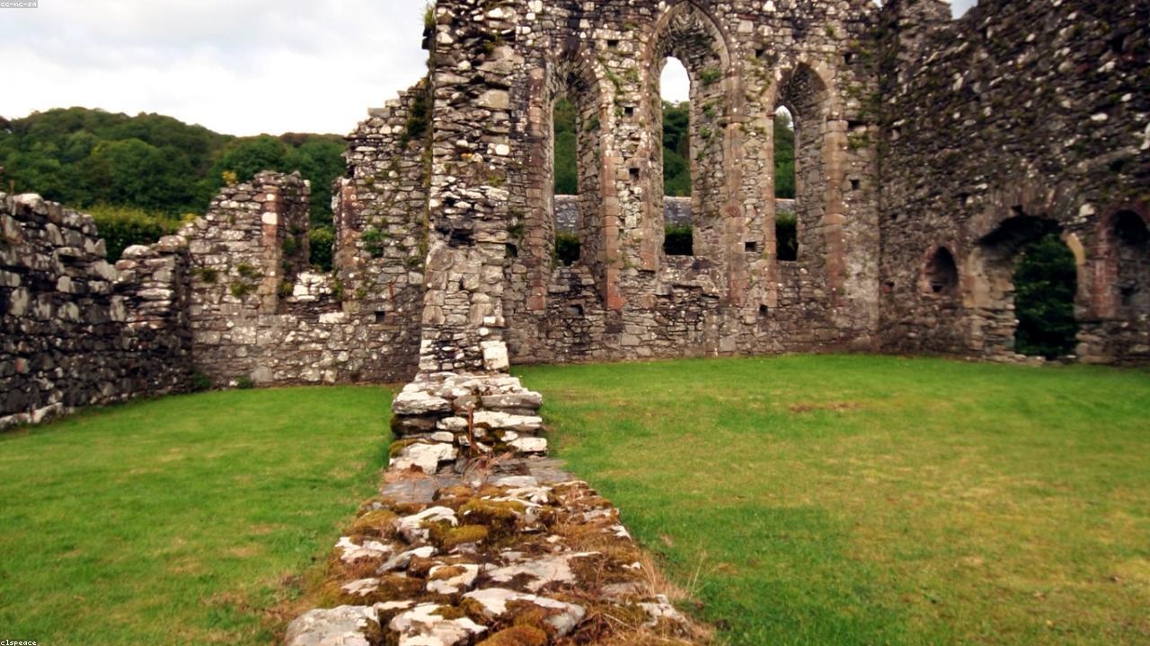 Cymer Abbey ruins in a flat river meadow below the hills of Snowdonia, the arched church windows standing against the mountains